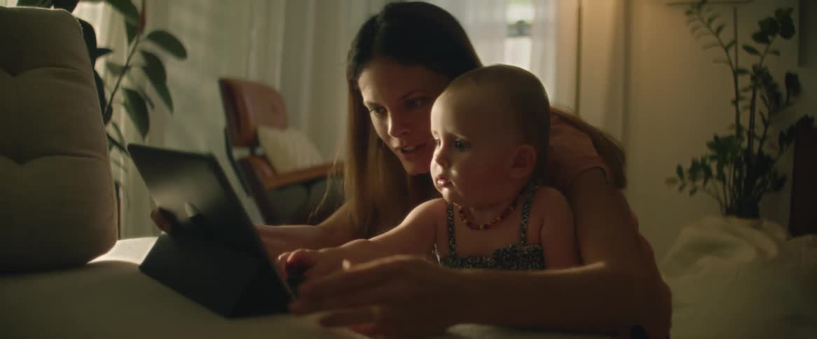 A woman is sitting at a table with her little girl letting her push the keys on a tablet computer keyboard