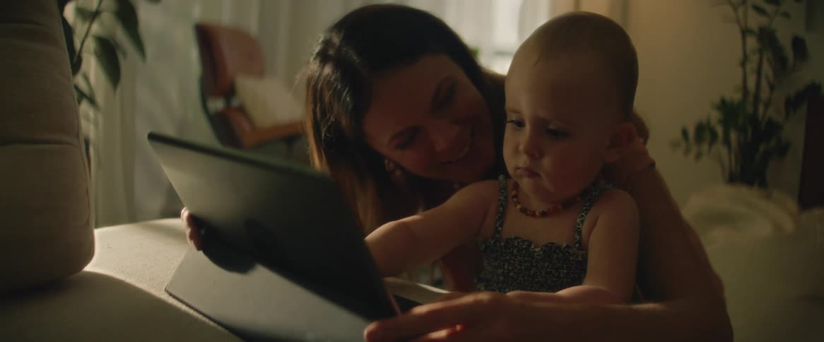 Mother holds infant daughter as the girl plays with a tablet