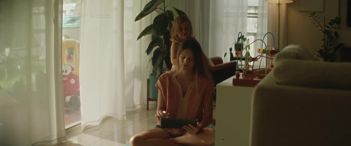 Mother talks to daughter and uses tablet while her daughter brushes her hair