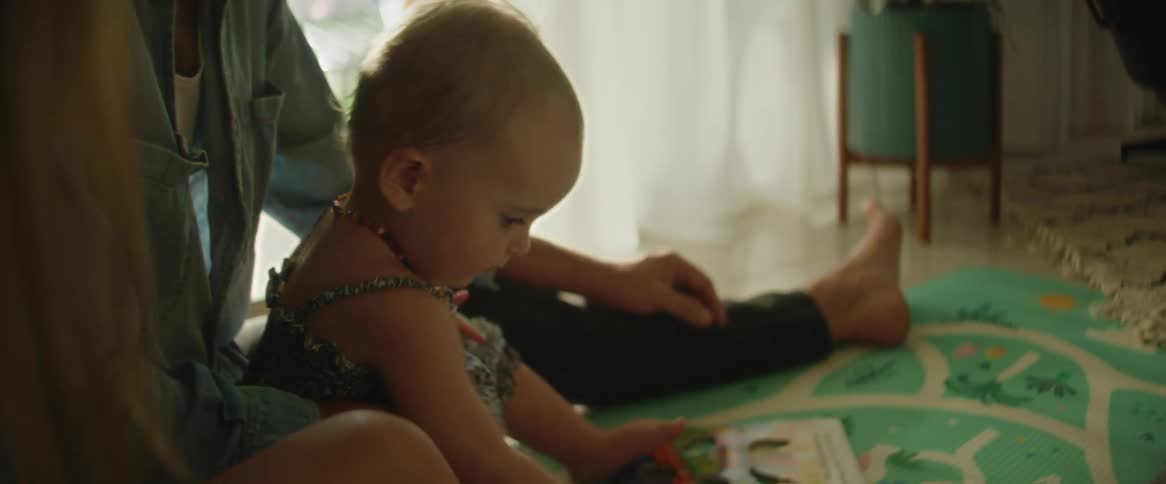 A father sitting behind his young baby daughter with mom next to them playing on the floor