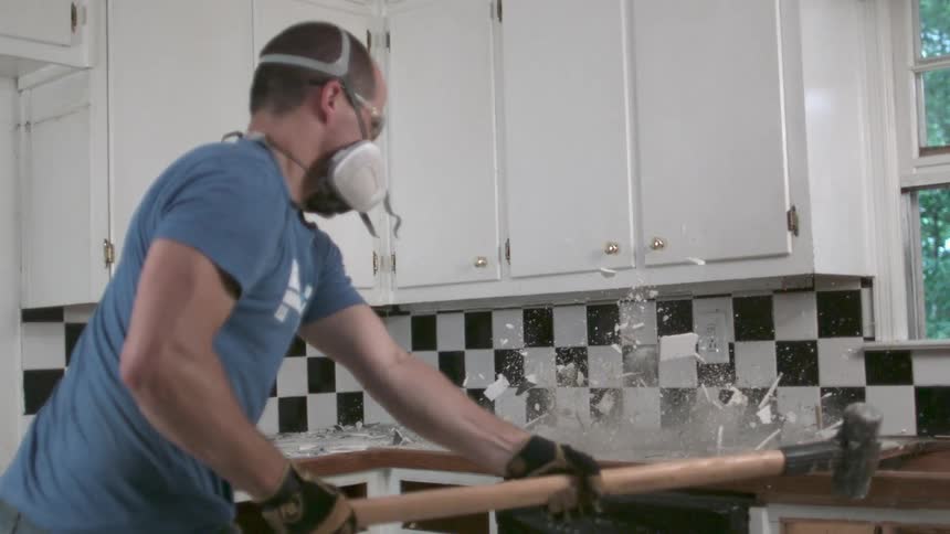 Man destroying a kitchen counter with a sledgehammer while wearing protective equipment