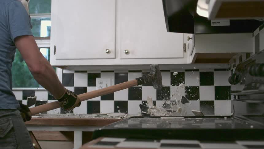 Man smashing a countertop with a hammer in a kitchen