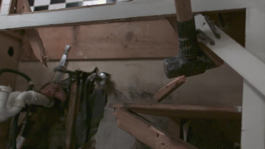 A sledge hammer is striking at the framework of a cabinet