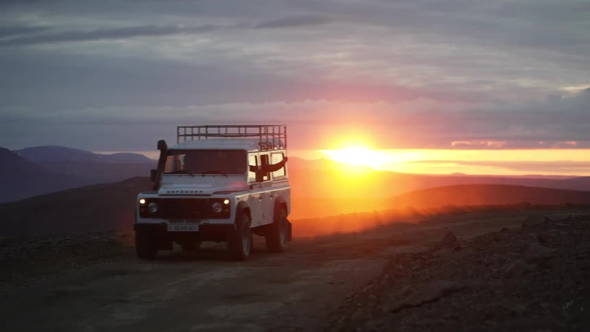 Driver gestures through the window while driving a vehicle along a dirt road during sunset
