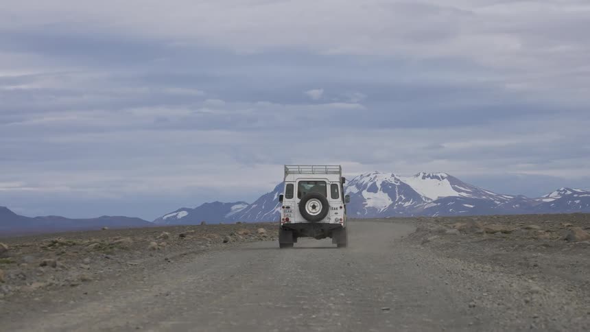 White offroad vehicle driving on a dirt road with mountains in the background and cloudy sky