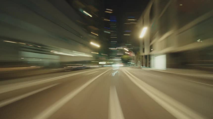 A hyperlapse rushes down a city street at night, streaking with speed and energy