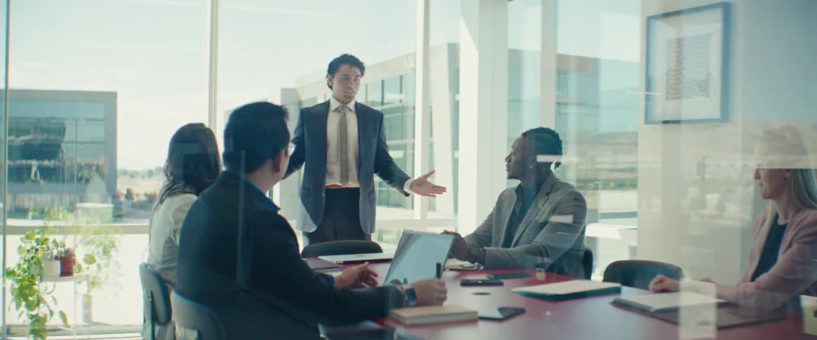 Colleagues gathered around a table in a modern office with large windows in a business meeting