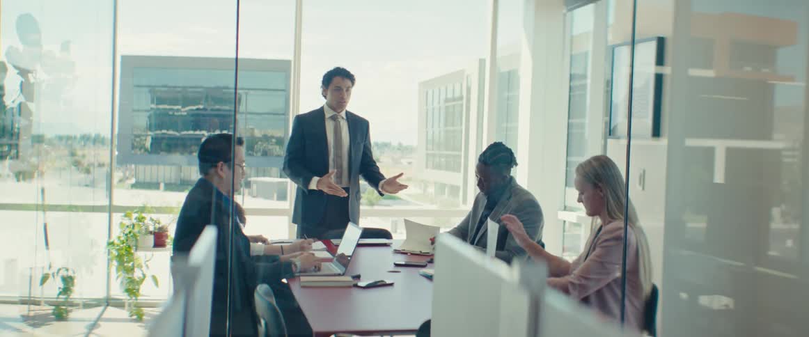 An asian man in a suit speaks to workers at an office meeting