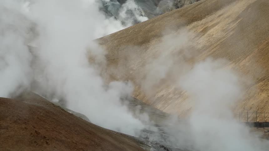 A person hikes on a geothermal area with steam vents on a mountainous terrain