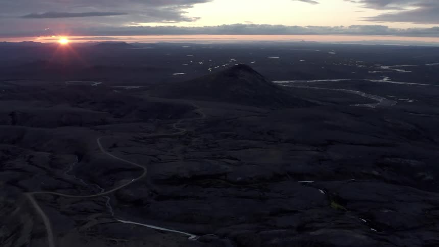 A sunset view over a rugged landscape with a prominent mountain peak and rivers