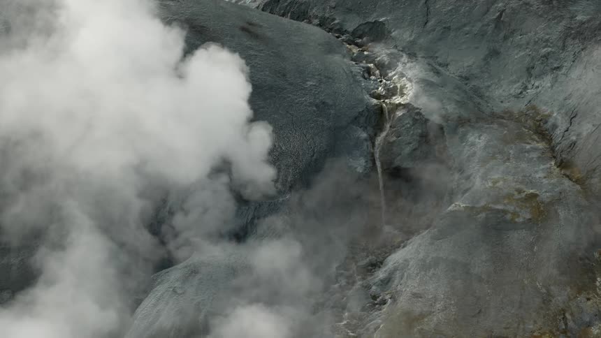 Geothermal area with steam vents and a waterfall on a mountainous terrain