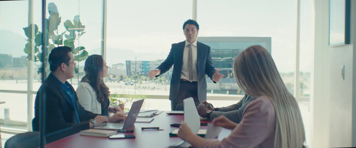 People sitting at a table with laptops and talking and interacting with a man in a suit who is standing and talking