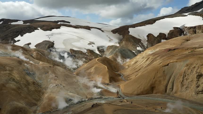 Geothermal area with steam vents and snow patches on a mountainous terrain