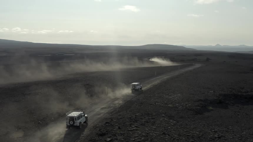 Vehicles stir the dust while traveling along a dirt road through the countryside