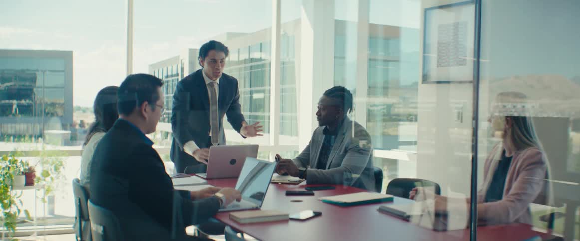 Colleagues gathered around a table in a modern office with large windows in a business meeting