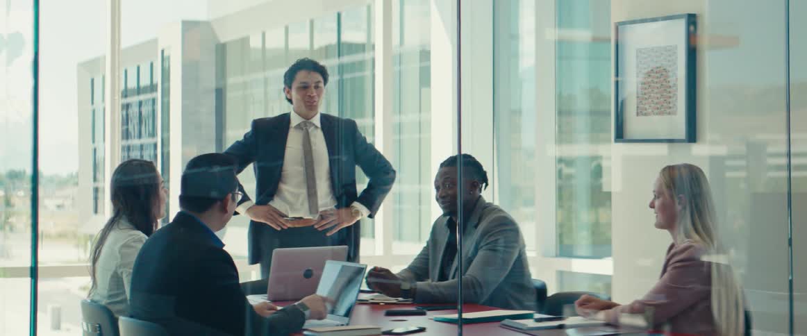 A man in a suit talks to four people sitting in an office