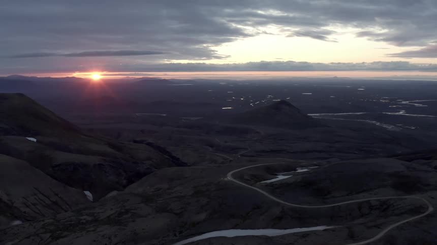 A sunset view over a rugged landscape with a prominent mountain peak and rivers