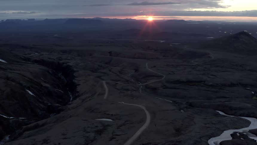 Aerial of a car travelling on a remote mountain road at dusk