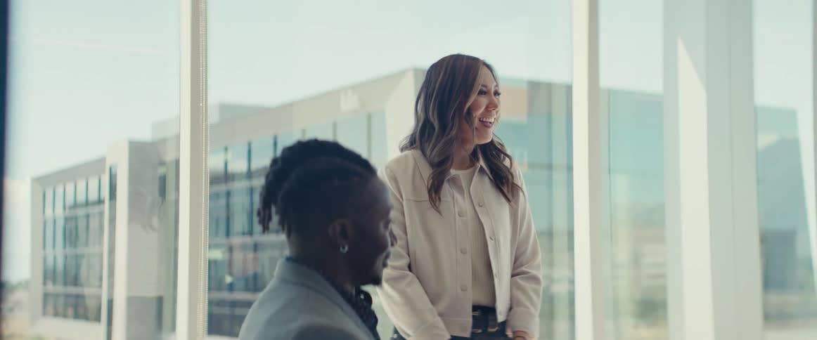 An asian smiles while standing next to a seated black woman in an office