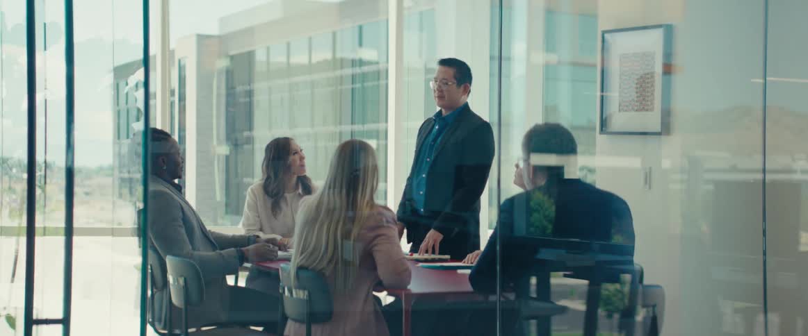 People in an office meeting talking with one man standing and the others sitting