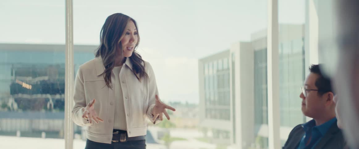 A woman in formal attire gives a presentation on a business meeting in a modern office with large windows
