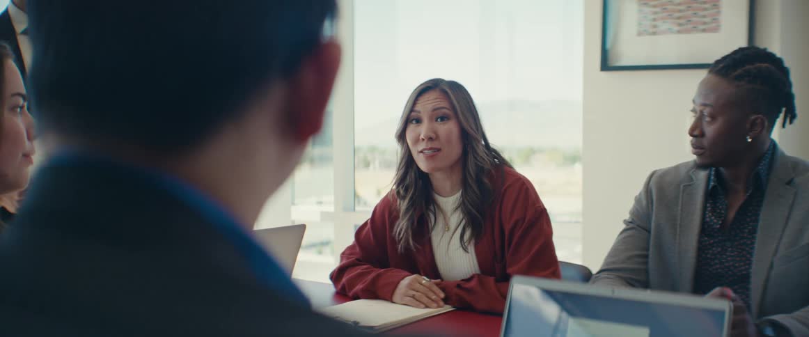 An asian woman talks to a group of colleagues in an office setting