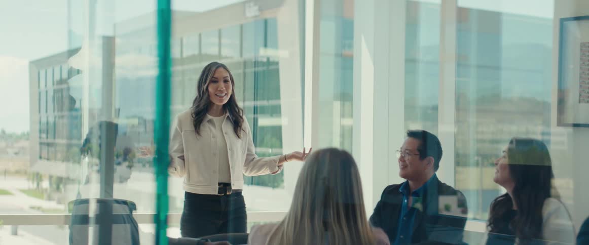 Woman standing in front of a table with other people sitting around talking in an office meeting