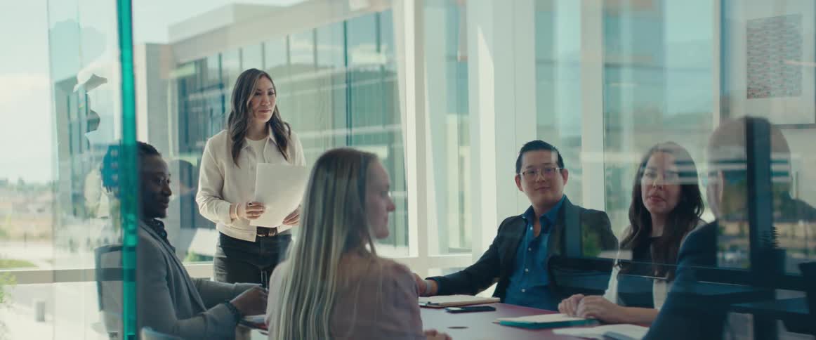 Woman standing talking to a colleague sitting at an office desk in a meeting