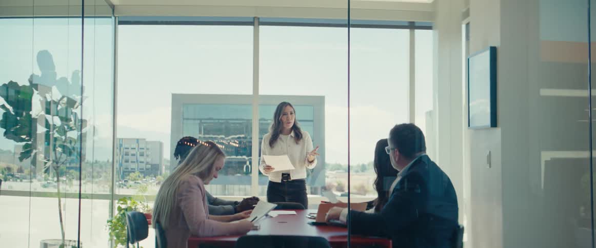 Colleagues gathered around a table in a modern office with large windows reviewing documents