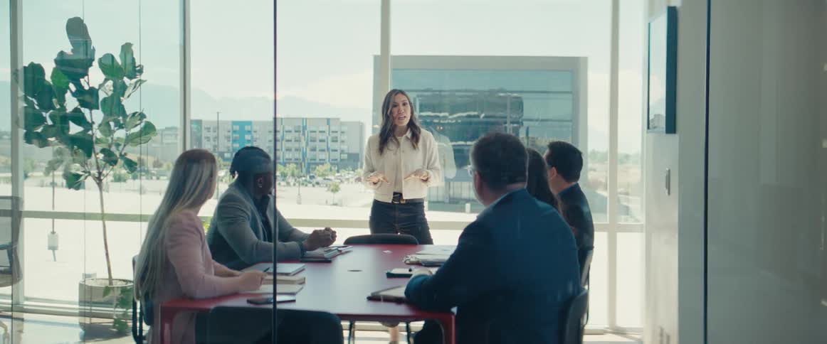 Woman standing and lecturing to other people who are sitting at an office desk