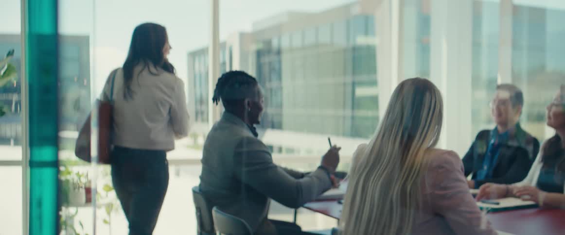 Woman arriving in a meeting room with other people sitting