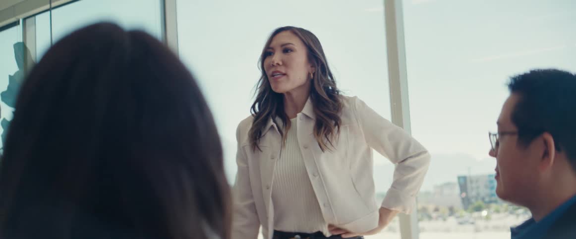 A woman in formal attire gives a presentation on a business meeting in a modern office with large windows