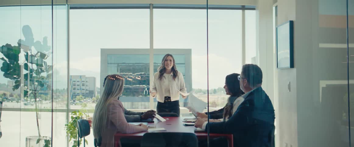 An asian woman walks into an office and begins speaking at a meeting