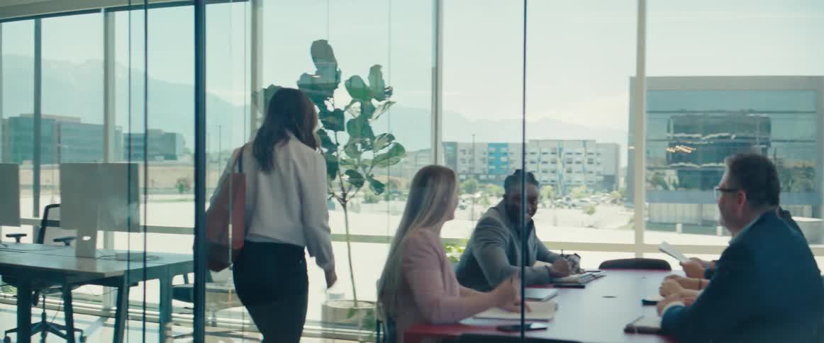 Woman walking into an office meeting with others sitting around a table