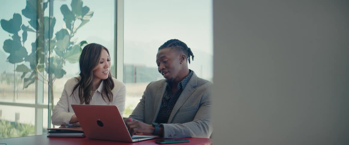 A woman and a man sitting at a desk discussing what theyre seeing in a laptop