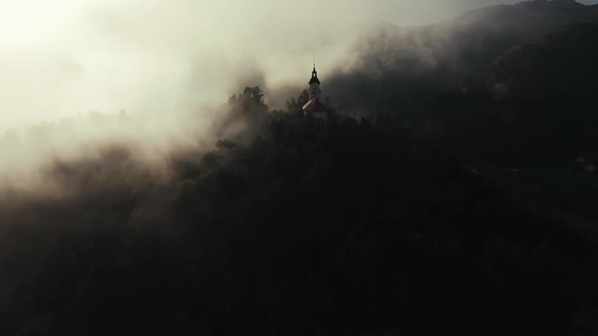A church sits on a mountain while fog hangs overhead