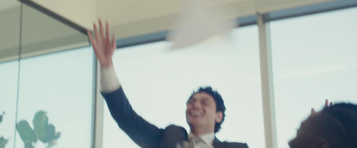 Man throwing papers in the air with people around him celebrating in an office environment