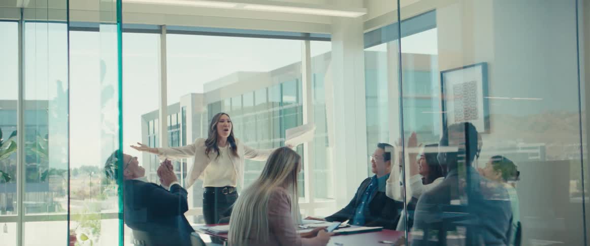 Woman standing at the head of a business office meeting talking vibrantly and excited.