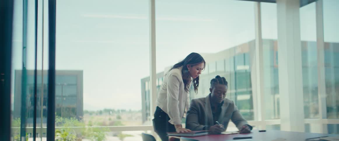 Woman standing next to a man sitting at an office desk