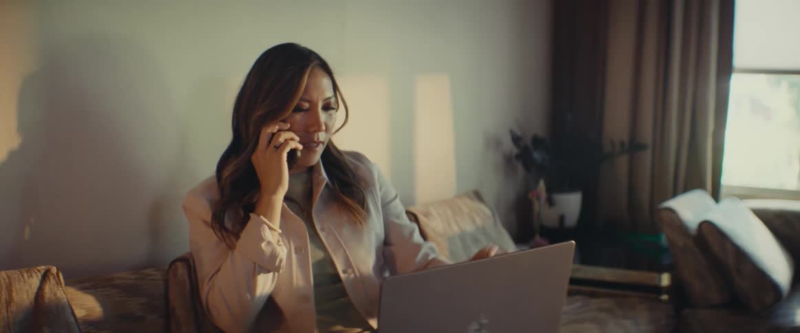A woman is talking on the phone while using a laptop