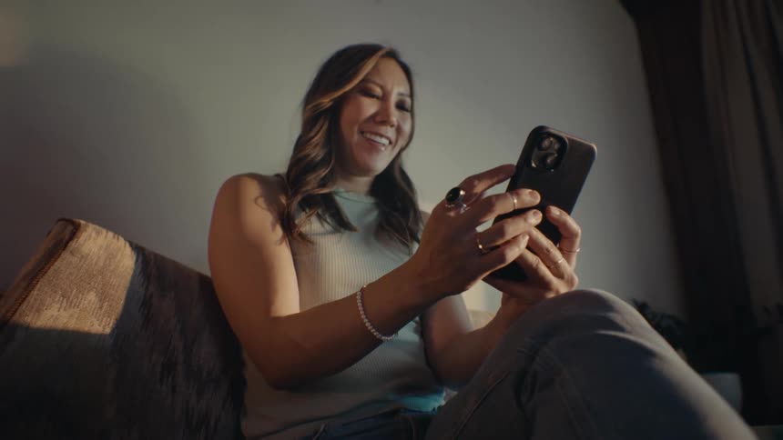 A woman sitting and smiling while looking at her smart phone