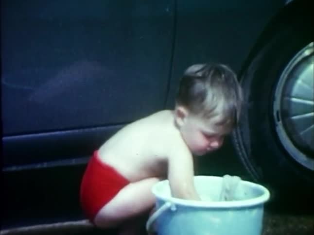 Little boy dunks a rag in a bucket of water