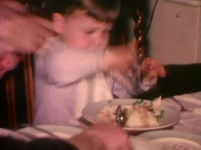A hungry little boy eats while adults serve food