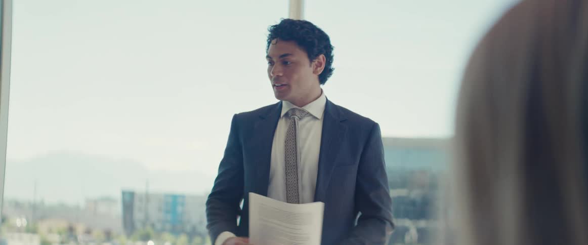 A man in formal attire gives a presentation on a business meeting in a modern office with large windows