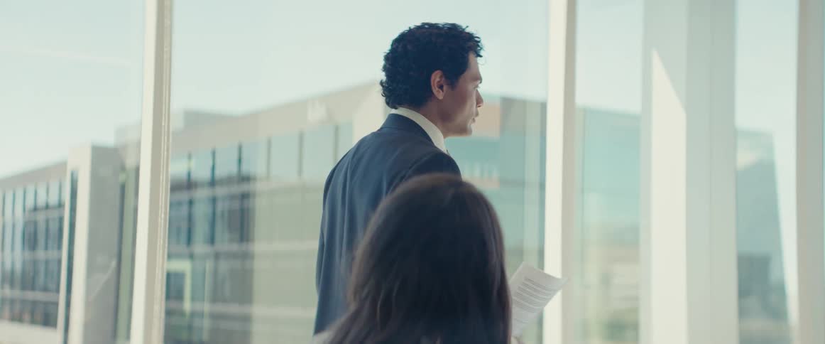 A man in formal attire gives a presentation on a business meeting in a modern office with large windows