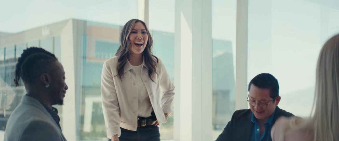 Group of people sitting at an office desk with a woman standing there laughing