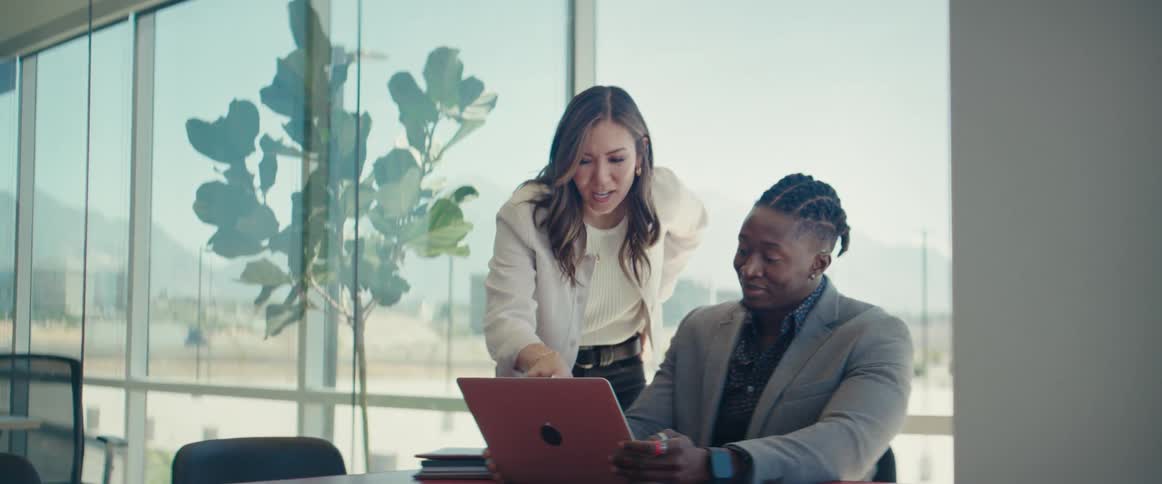 Woman standing talking to her colleague who is in front of a laptop at an office desk