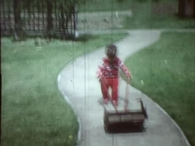 A toddler wearing red pushes a lawnmower