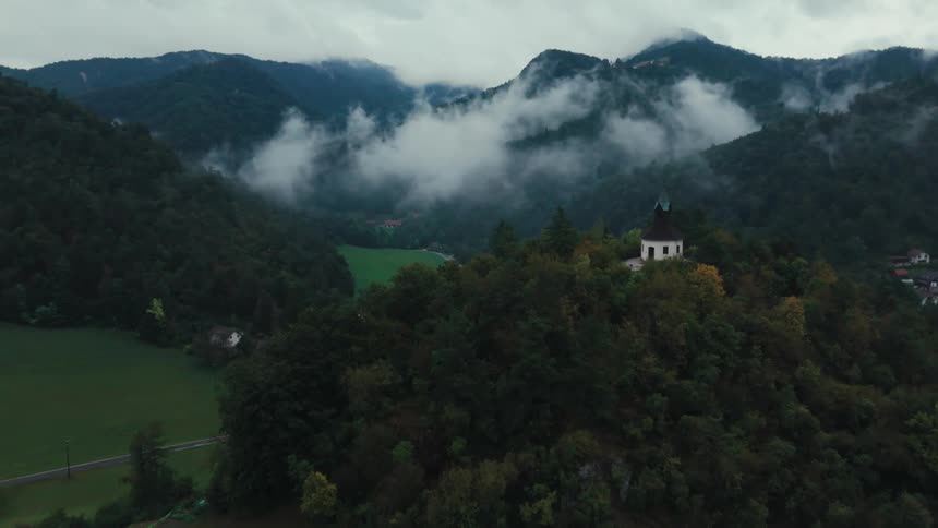 Aerial view of a church on a hill surrounded by forests on a cloudy day