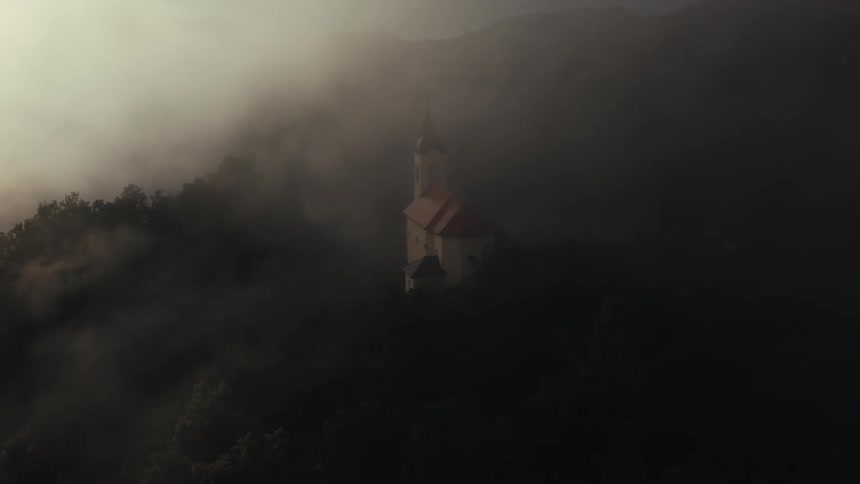Aerial panorama and a church on a wooded hill with fog around it